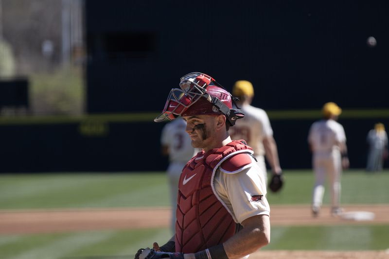 A smiling catcher in red gear walks off the field