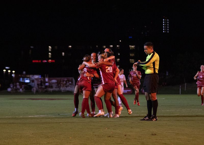 Soccer players hug after a goal at night as the referee walks past