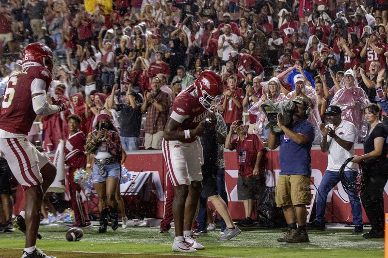 Football players celebrate in the end zone in front of camera operators and fans in rain ponchos